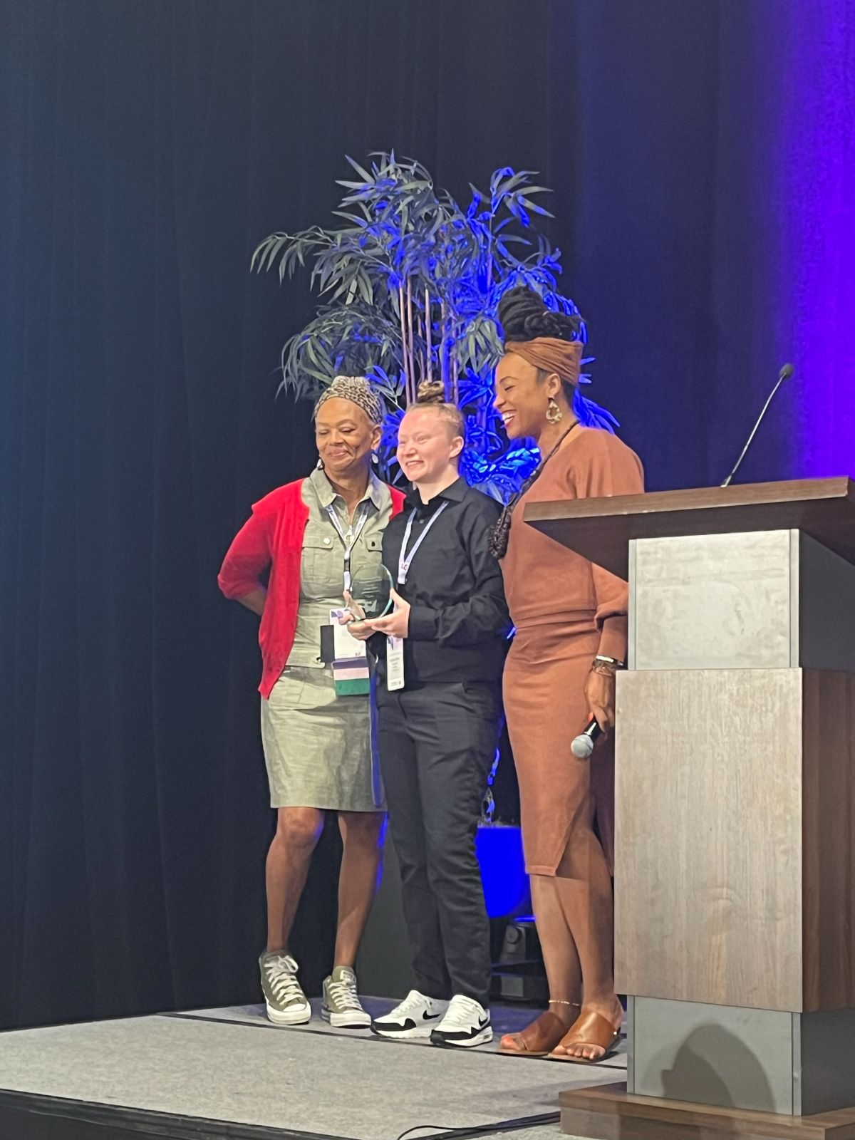 Kristina Tanner receiving an award and posing for a picture with two women near a podium