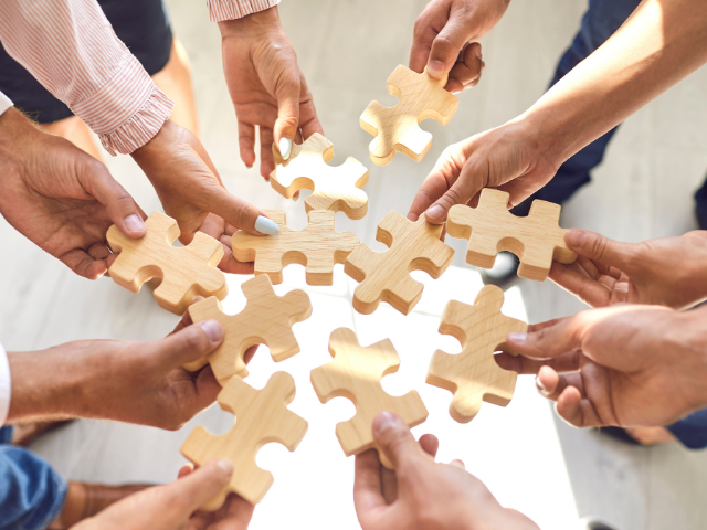Several hands holding wooden puzzle pieces joining into a circle, teamwork.