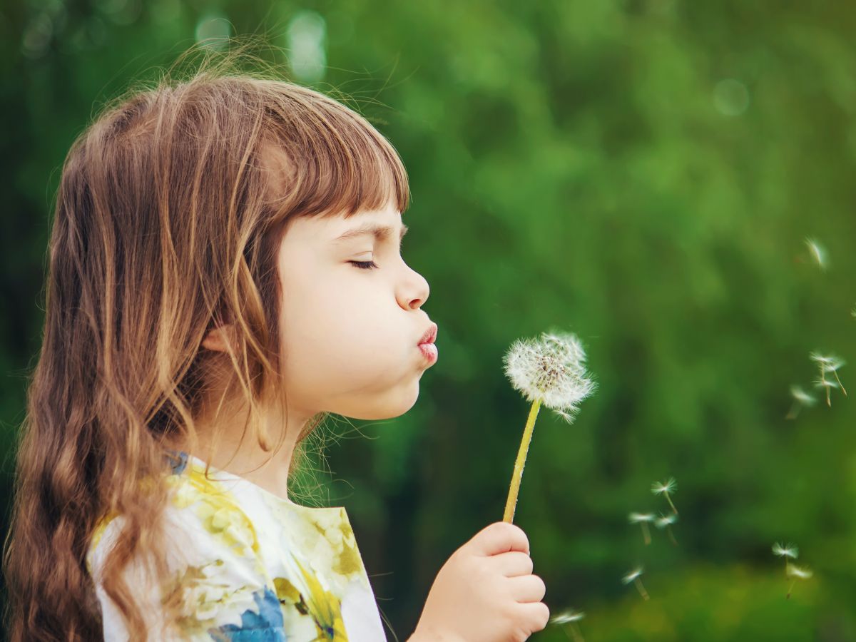 Young girl blowing dandelion seeds outdoors, soft green background