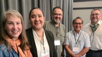 Five smiling adults with conference badges standing shoulder-to-shoulder indoors