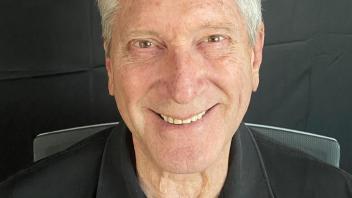 Smiling man with gray hair in black polo, studio headshot