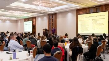 2025 Title Four E Summit participants gather in a large banquet room while a presenter, Avni Panchal, gives a presentation from a raised stage at the front of the room.
