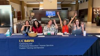 Smiling UC Davis staff at registration table waving in lobby