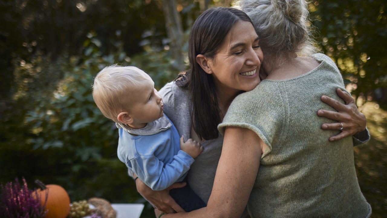 A baby, being held by a woman who is embracing an older woman