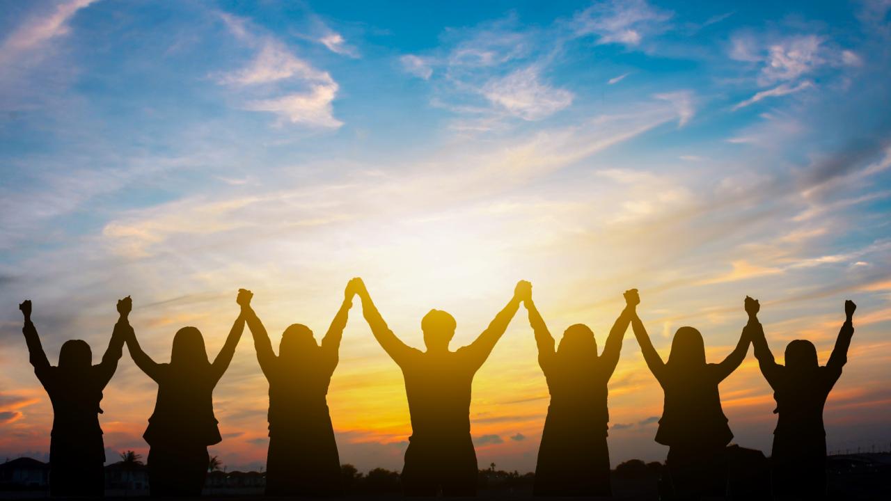 Silhouetted people holding hands, cheering at colorful sunset sky
