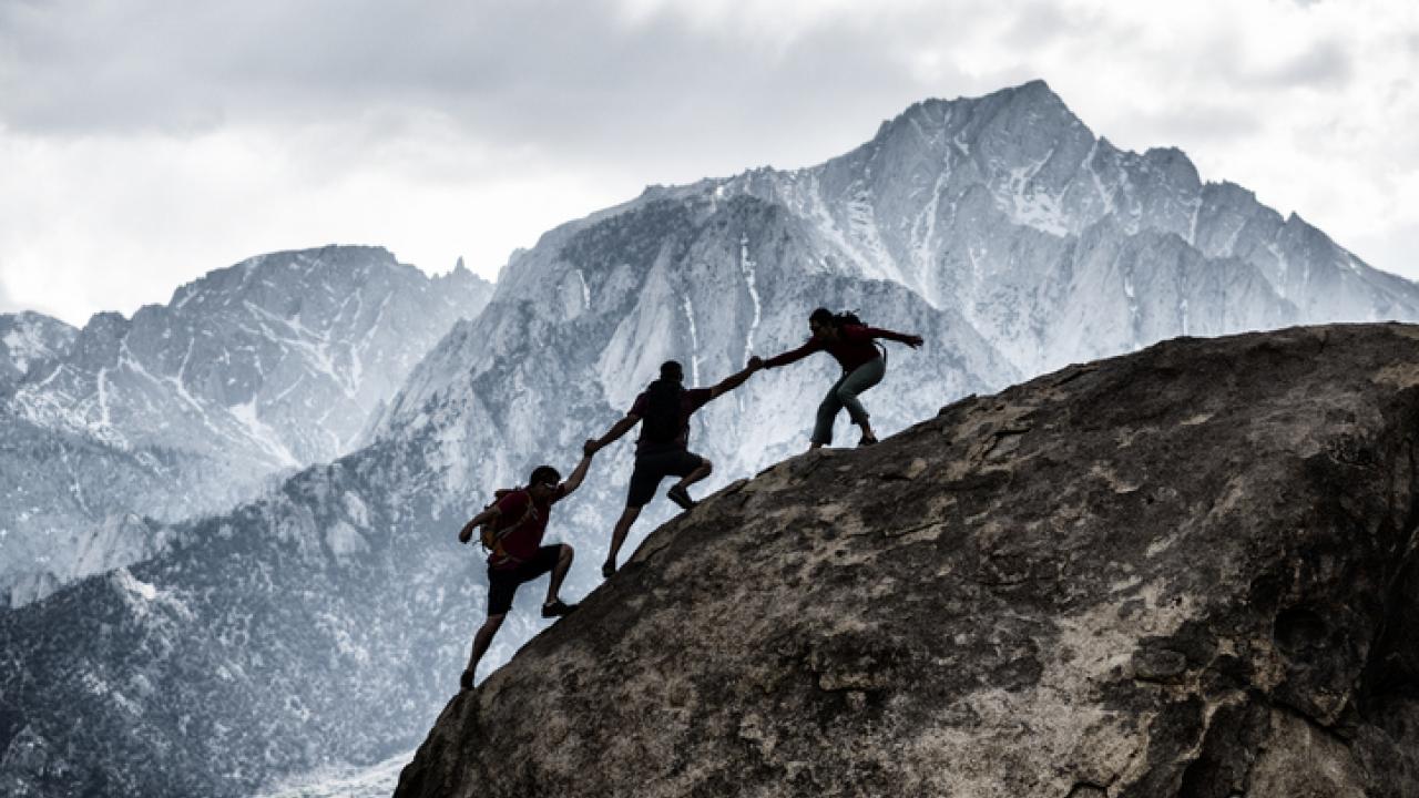 Three fellow mountain climbers helping one another ascend.