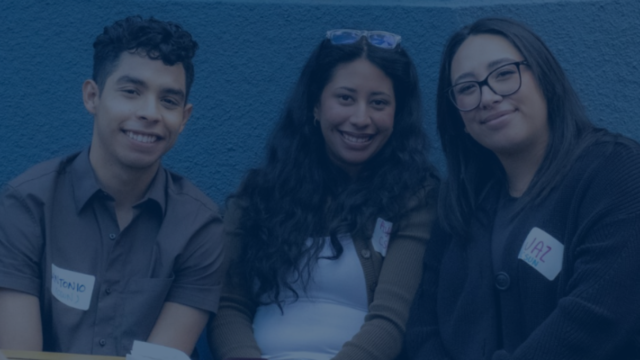Three students, one young ban and two young women, smile for a photo against a blue background.