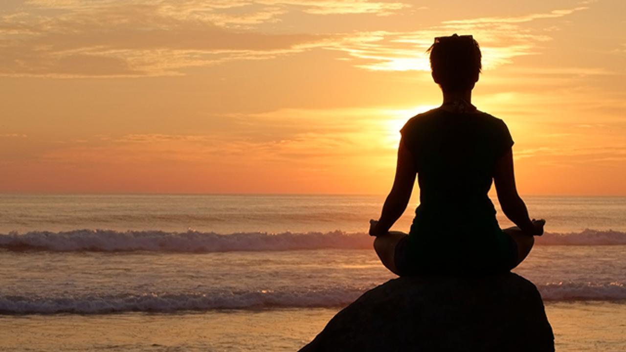 woman sitting on rock on beach looking at sunset