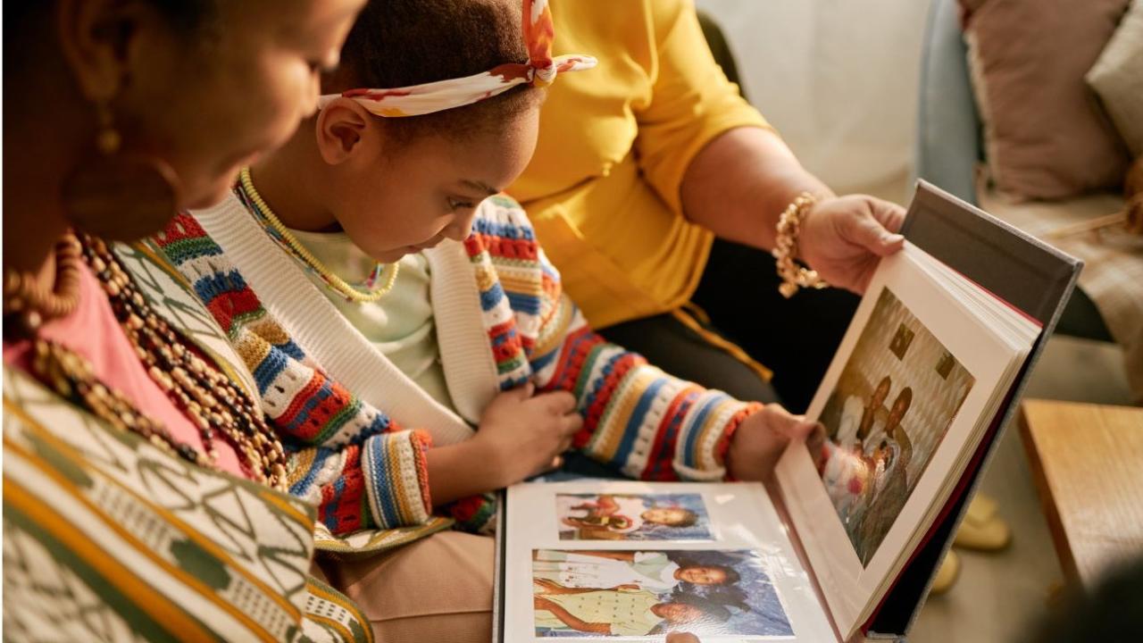 Three-generation family on sofa smiling as they browse a photo album.