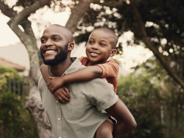 A smiling father giving his happy son a ride on his shoulders.
