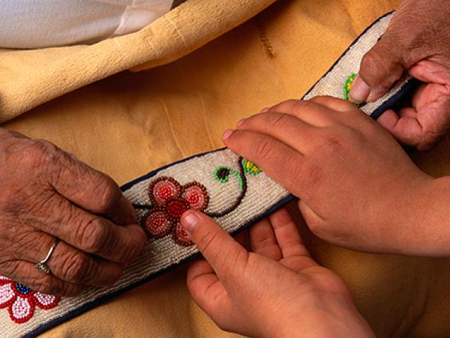 Tewo sets of hands, one older and one younger, working collaboratively on a craft