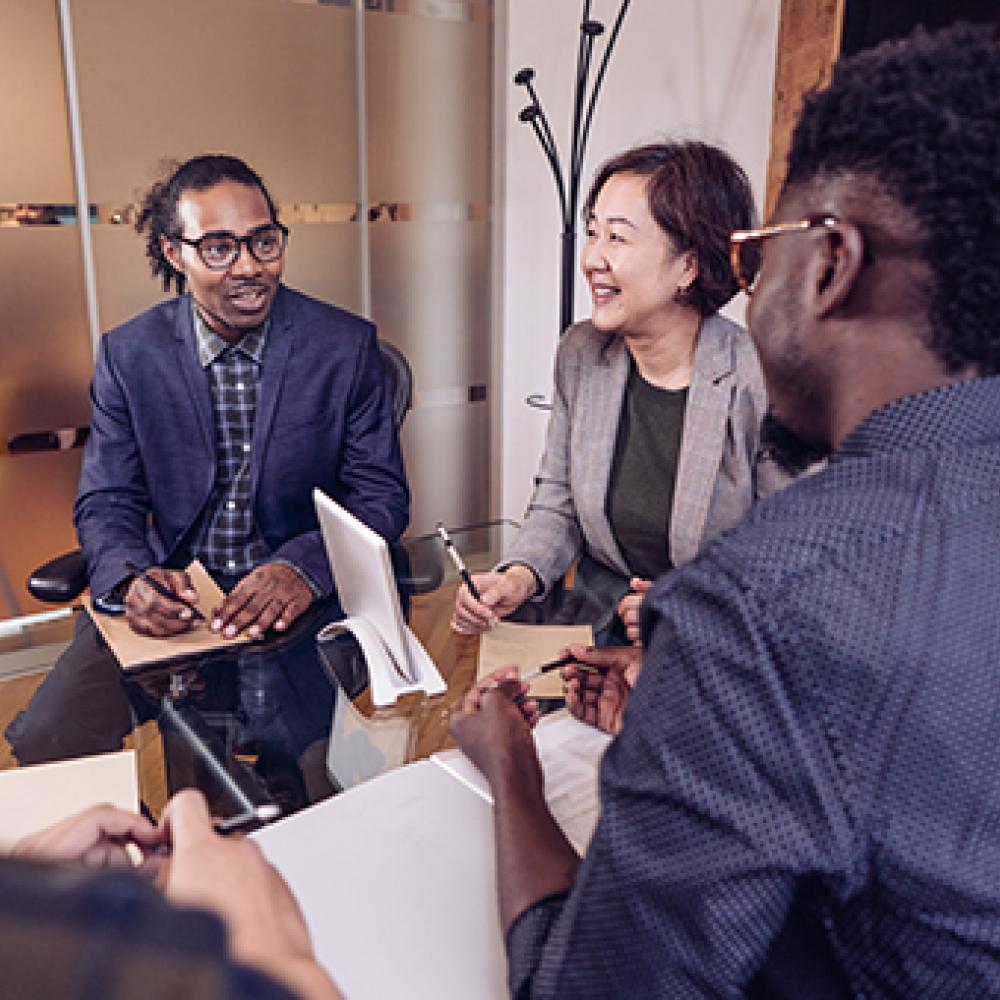 Four colleagues in a bright office, smiling and discussing around a laptop