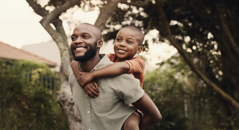 A smiling father giving his happy son a ride on his shoulders.