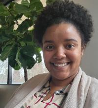 Smiling Black woman with short curly hair and cardigan, indoor plant behind