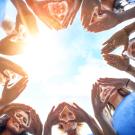 A circle of smiling people looking down at the camera, making heart shapes out of their hands.