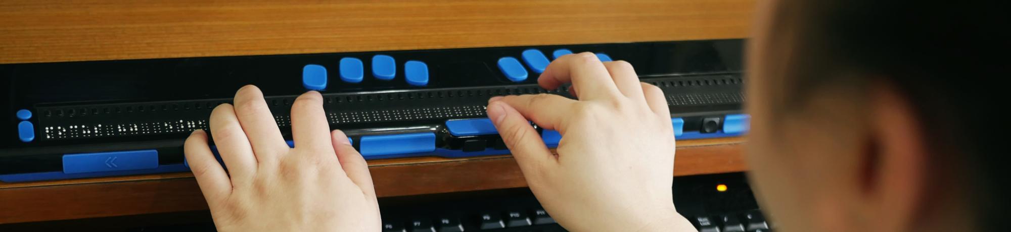 Rear view of person with blindness disability using computer keyboard and braille display or braille terminal a technology assistive device for persons with visual impairment
