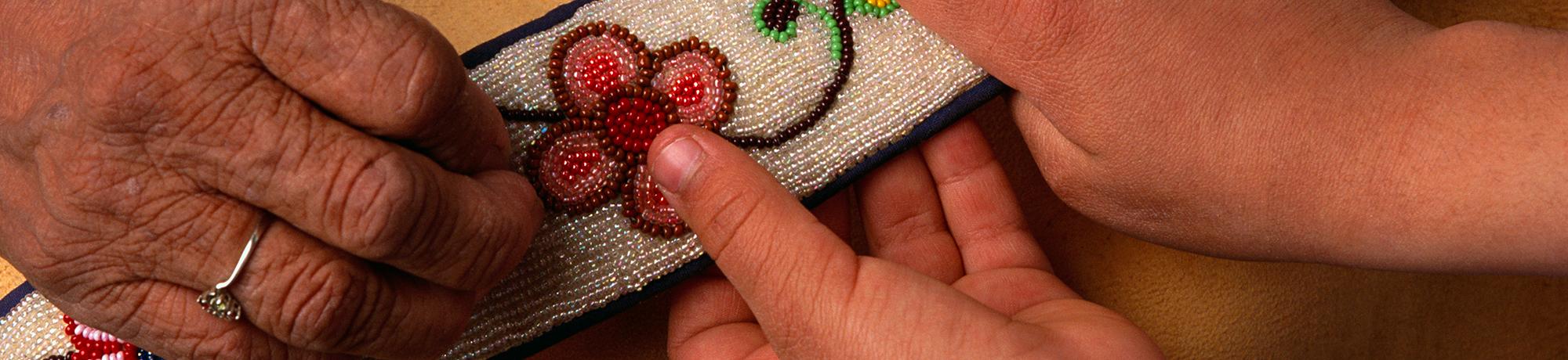 adult hands and child hands holding a beaded cloth